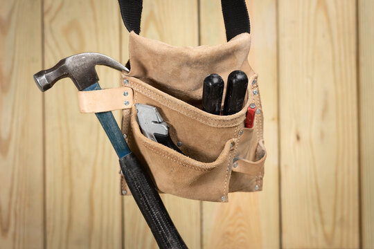 Tool belt with hammer and other tools hanging in front of a wood plank background