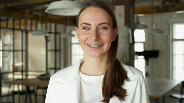A happy young woman in braces smiles in the office, looking at the camera.