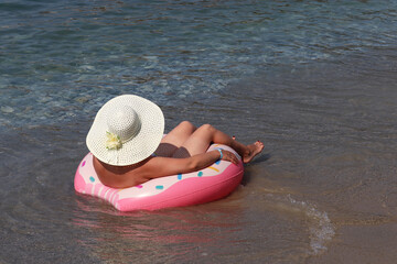 Woman in sun hat swimming on inflatable donut ring in the sea waves. Beach vacation, summer holidays