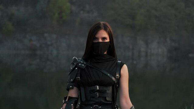 Portrait fantasy woman warrior assassin holds dancing with two burning blade daggers in hands, flame fire. Dancer hiding face behind mask. Armed sexy girl. Black costume. Halloween concept 4k footage