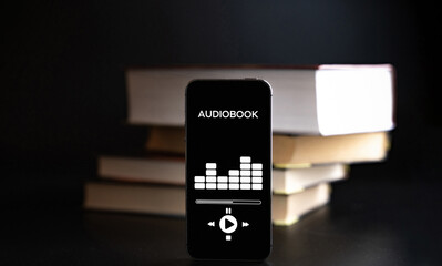 Audiobooks concept. Smartphone screen with audiobook application on paper books black background. Concept of education, library, students.