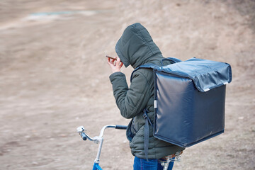 Bicycle food delivery service, courier on bicycle deliver food. Delivery person with thermo backpack checking order using smartphone. Pizza delivery, courier with food backpack go to customer.