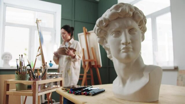 A woman artist painting standing by the easel - marble bust on the foreground