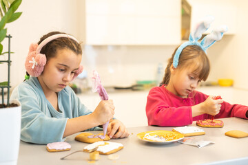 Fototapeta premium Two girls decorate cookies on plates with chocolate icing. Cooking treats for halloween celebration. Lifestyle