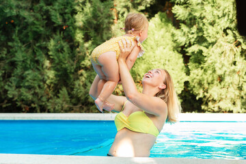 Fototapeta na wymiar Summer vacation. Portrait of happy mother plays with her little daughter in the pool. International Children's Day