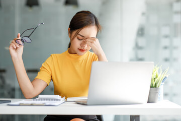 Asian women sitting in an office With stress and eye strain Tired,
portrait of sad unhappy tired frustrated disappointed lady suffering from migraine sitting at the table, Sick worker concept