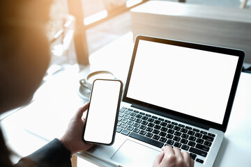 mockup image computer,cell phone blank screen for hand typing text,using laptop contact business searching information in workplace on desk at office.design creative work space on wooden desk.