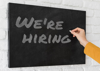 Hand with chalk writing We're hiring on black chalkboard