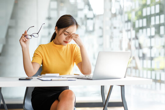 Asian Women Sitting In An Office With Stress And Eye Strain Tired,
Portrait Of Sad Unhappy Tired Frustrated Disappointed Lady Suffering From Migraine Sitting At The Table, Sick Worker Concept