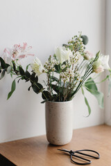 Stylish bouquet in ceramic vase on wooden windowsill. Beautiful fresh flowers and scissors on wooden background, floral arrangement. Spring modern bouquet