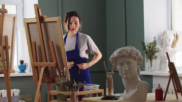 A woman artist ties an apron on herself and starts painting on canvas