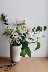Stylish bouquet in ceramic vase on wooden windowsill. Beautiful fresh flowers and scissors on wooden background, floral arrangement. Spring modern bouquet