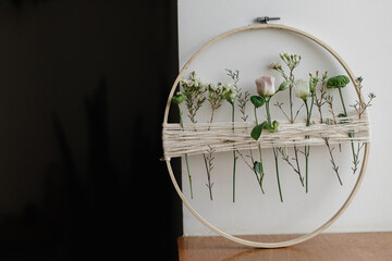 Stylish spring boho wreath with beautiful fresh flowers. Wooden hoop with flowers and thread on white wall background. Modern and creative floral handmade decor. Space for text