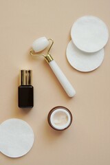 Skin care products, antiaging cosmetics, quartz face massage roller, facial cream, serum, cosmetic pads, aesthetic flat lay composition, vertical image. 