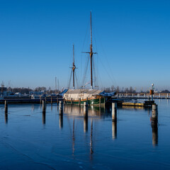 Fototapeta na wymiar A sailboat in a marina closed down for winter. Blue water and a clear blue sky