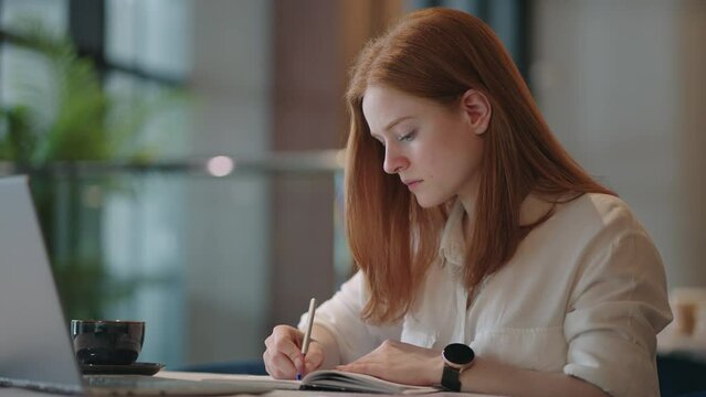 young female writer is working alone at home, making notes in book, journalist freelancer is writing