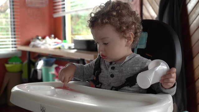 little caucasian latino baby sitting and sipping a drink in his dining chair at home