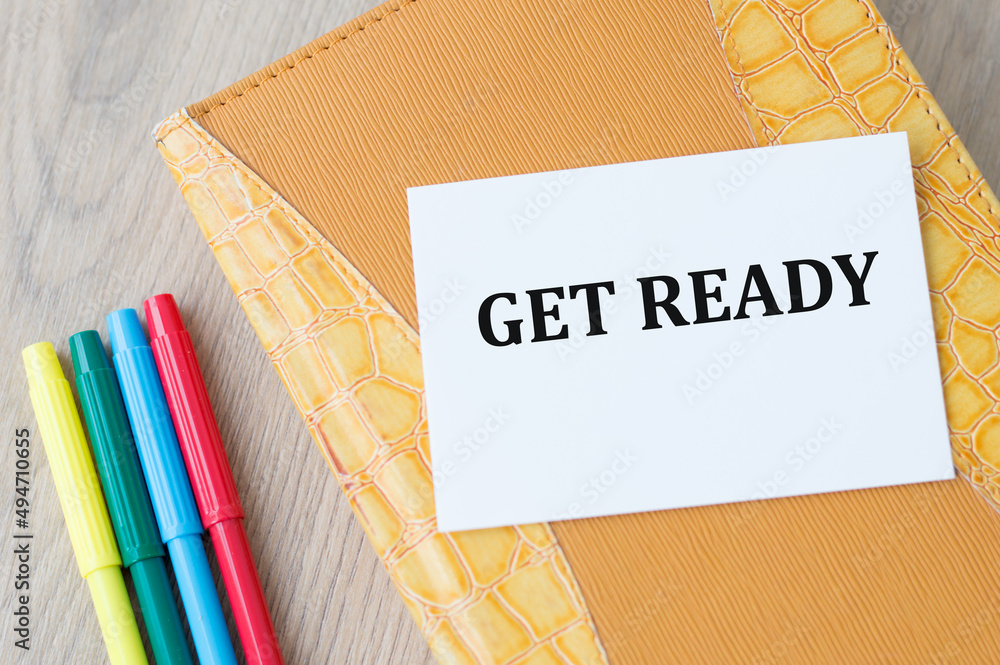 Poster get ready text on a card against the background of a yellow notebook on the table next to the colore
