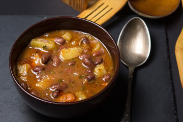 Bean soup with meat in a plate on a black background. Traditional food. Delicious and nutritious lunch