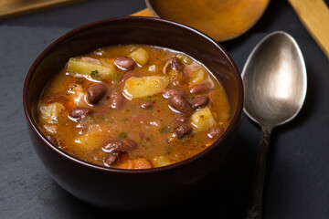 Bean soup with meat in a plate on a black background. Traditional food. Delicious and nutritious lunch