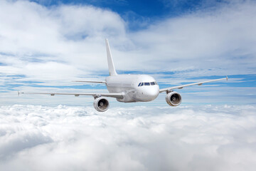 Fototapeta na wymiar White airplane flies along the edge of the clouds above.