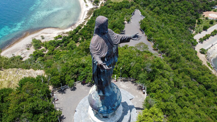 The famous statue of Jesus Christ, Cristo Rei, surrounded by greenery and crystal clear turquoise ocean in capital Dili, Timor Leste, aerial drone view