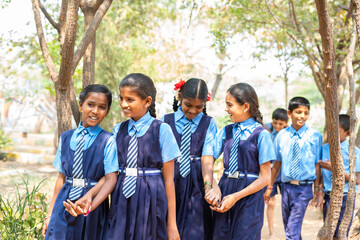 Group of teenage kids in uniform holding hands while going to playground at school - concept of...