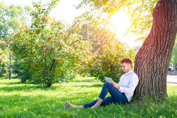 Young man using tablet computer under tree