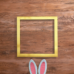 White pink bunny ears under a gold frame on a wooden background. Text space. Top view. Minimal style.