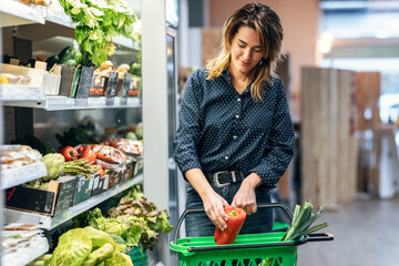 Beauty woman walking with shopping cart while taking products from shelf at the grocery