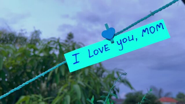 I LOVE YOU MOM. A love confession to a parent hanging on a rope at cemetery in colorful neon light. Feelings of affection and happy memories of those who passed away.