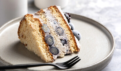 Diet dessert close up. Piece of vanilla biscuit cake with cream, blueberries and blackberries close-up on a ceramics plate on a light gray concrete background