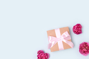 Present with a tied ribbon and heads of rose flower on a blue pastel background. Gift for a Mothers Day. Congratulation concept.