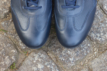 Navy blue leather shoes for men on footpath made of rocks or stones. Male footwear