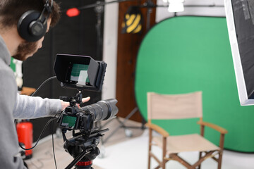 young man video camera operator making interview in professionnal broadcast tv movie studio film production with a green chromakey background