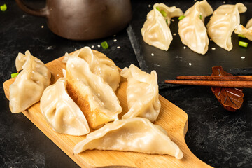 Gyoza on a wooden board, dark table. Chinese cuisine.