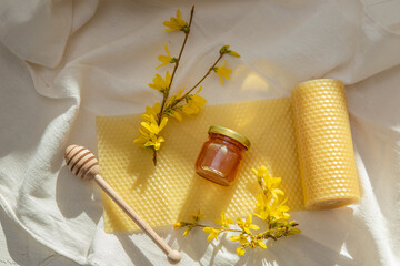 Jar of honey, natural wax candle made from beeswax plates, blooming forsythia sprig and honey dipper