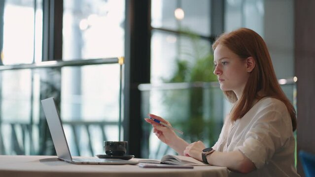 young woman is learning foreign languages online, listening to lecture by laptop and making notes in exercise book