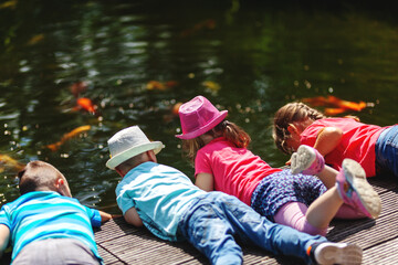 4 Kinder liegen auf einem Steg am Teich, planschen im Wasser und spielen mit Zierfischen