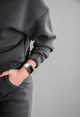 close up teen female hand with an electronic watch in gray oversize hoodie pocket near gray wall background. sport lifestyle concept, free space