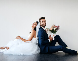 You can lean on me any day. Studio shot of a newly married young couple sitting back to back on the...