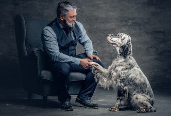 Old man shaking paw of his dog sitting on armchair