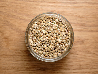 Hemp seeds, edible cannabis production. Marijuana grain in a round glass bowl on wooden texture background.