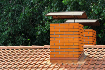 chimney made of new brick and a tiled roof on a background of tree leaves