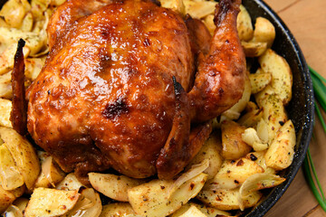 roasted potatoes and baked chicken meat in a frying pan, cooked food, delicious crust, one object on a wooden background