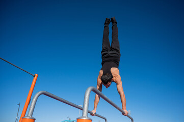 Shirtless man doing handstand on parallel bars at sports ground. 