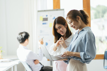 Fototapeta premium Two asian female collegues standing next to each other in an office, business meeting discussion concept.