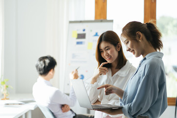 Two asian female collegues standing next to each other in an office, business meeting discussion concept.