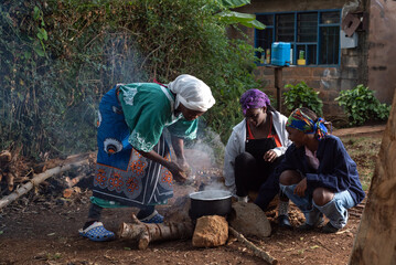 Older African Woman helping young teenage girls to  prepare a pot of tea