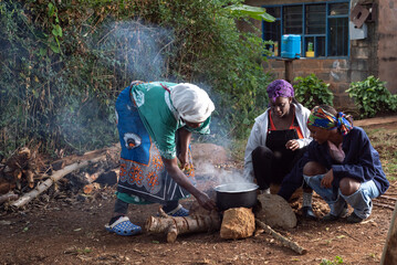 Older African Woman helping young teenage girls to  prepare a pot of tea